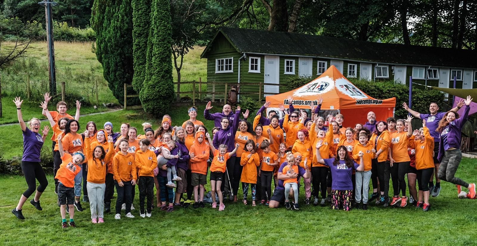 Group of about 50 children and young people in orange t-shirts with adult volunteers attending a Fab Camp activity holiday for bereaved military families