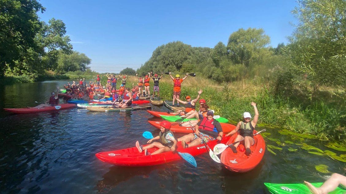 Group of children and young people attending FAB activity camp learning to kayak on sunny river