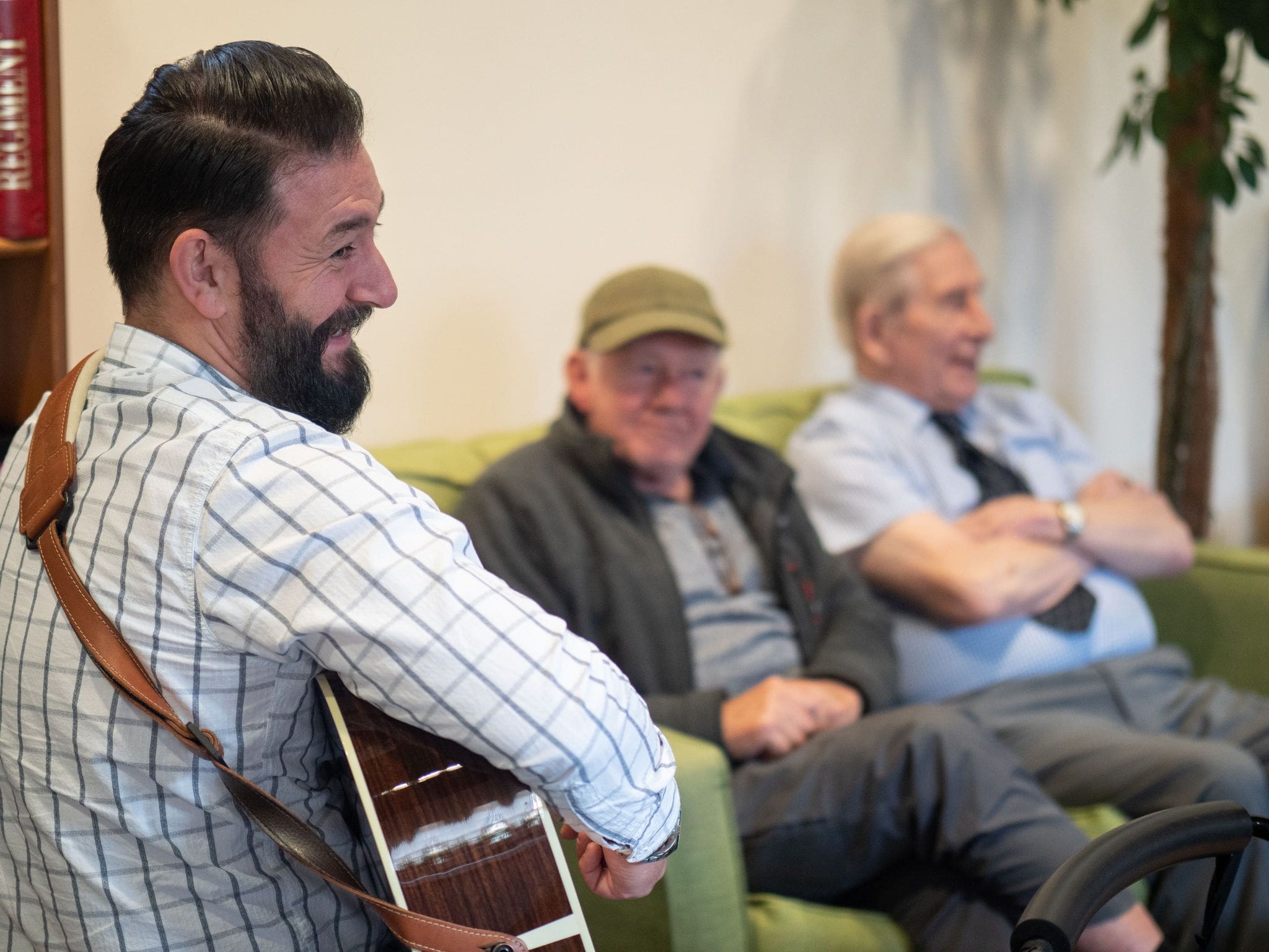 Man with beard smiling while playing guitar to two older men