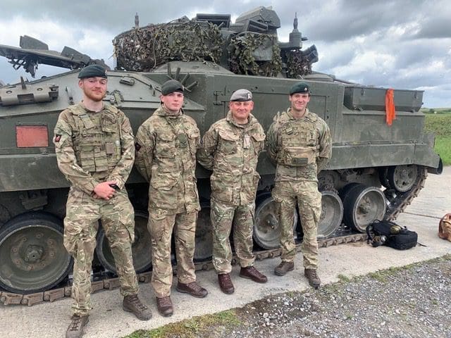 4 soldiers stand in front of Warrior tank