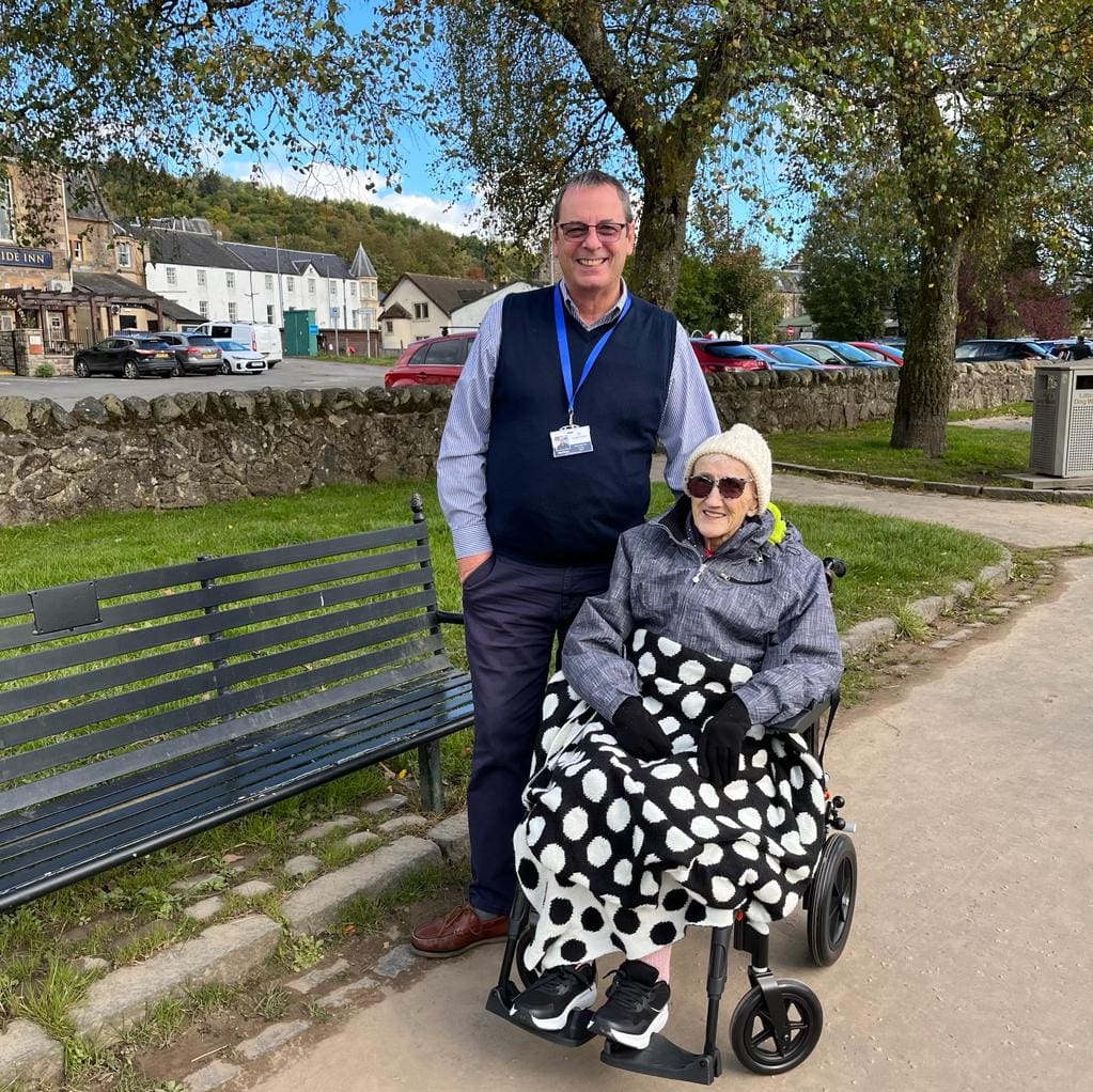 Elderly woman in a wheelchair, accompanied by male volunteer