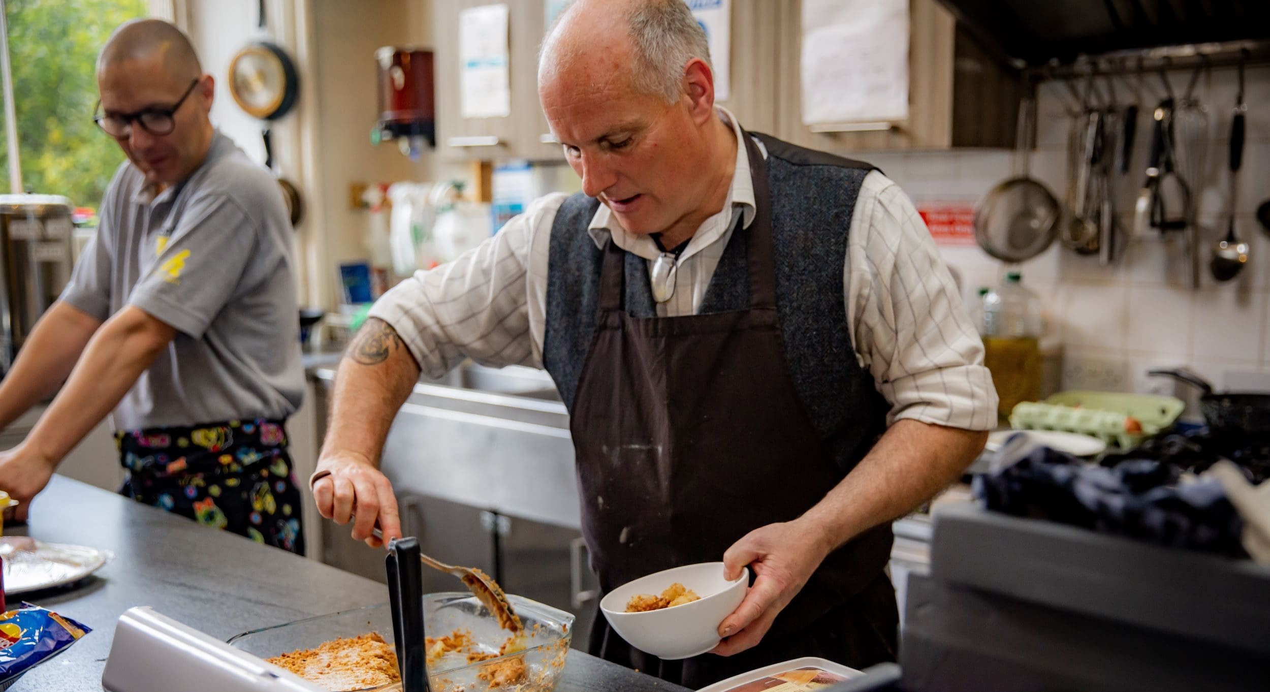 Bald man in waistcoat cooking in premises kitchen