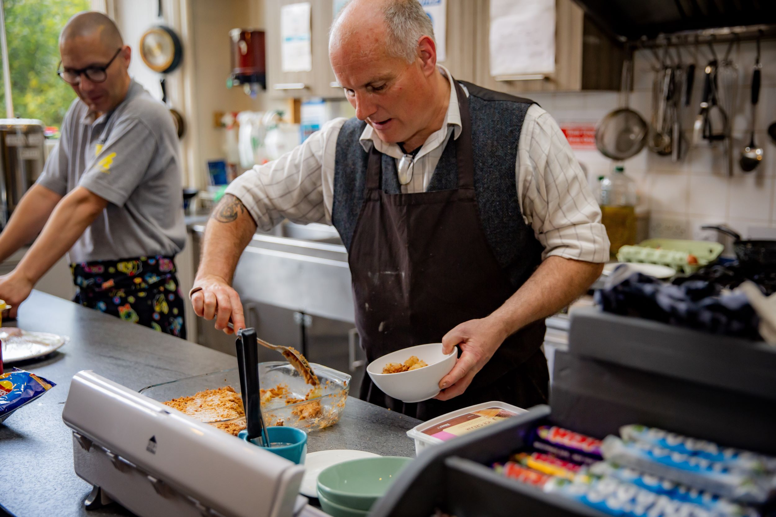 Bald man in waistcoat cooking in premises kitchen